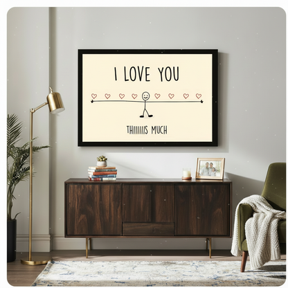 Black framed funny love quote stick figure canvas art hung above a dark walnut sideboard with stacked books and family photo frame in a modern living room with gold floor lamp and olive green chair