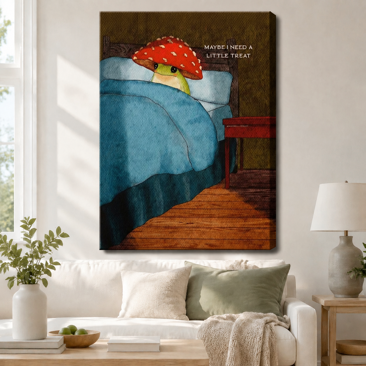 Gallery wrap canvas of a cute frog with red amanita mushroom hat in bed, "Maybe I Need A Little Treat" quote art hung above a white sofa in a cozy living room