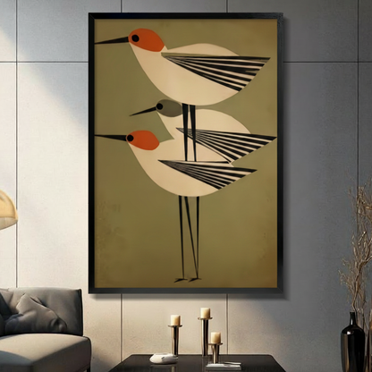 Framed mid-century modern bird trio canvas wall art with three geometric shorebirds in orange and black striped wing design on olive green background in a modern living room