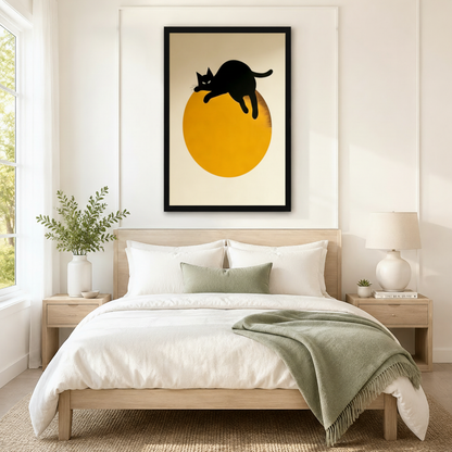 Black framed mid-century minimalist black cat moon canvas art with a bold black cat silhouette lazily draped over the top of a large golden amber circle with all four legs dangling and tail softly curled upward and a cool piercing gaze on a clean warm off-white background in a striking minimal black gold and cream palette, hung above a light wood bed frame in a serene Scandinavian bedroom with crisp white linen bedding, a sage green throw blanket, matching wood nightstands, a white ceramic table lamp