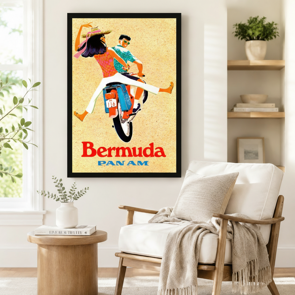 Large black-framed vintage Pan Am Bermuda travel poster print with a couple on a moped, styled beside a linen armchair and round side table in a Scandinavian reading corner