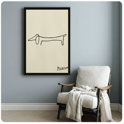 Picasso minimalist one-line dachshund drawing with handwritten signature gallery wrap canvas art on cream background on a dark gray paneled wall above a charcoal sofa with candle holders and a black vase
