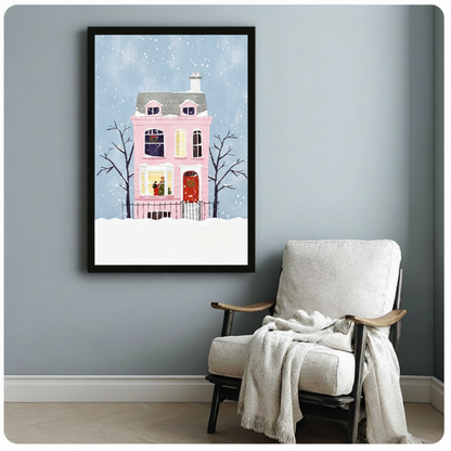 Whimsical flat illustration of a pink Victorian house with a red door and wreath surrounded by bare trees in falling snow Christmas wall art framed print beside white armchair on blue-gray wall