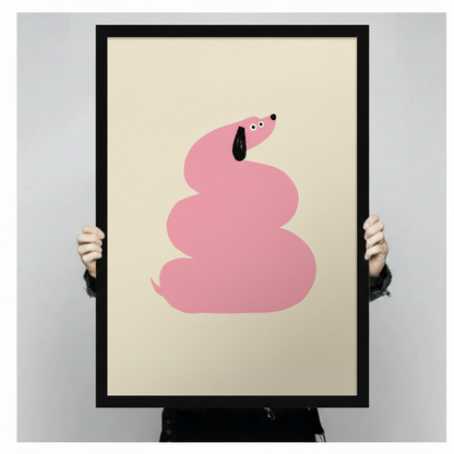Hand-held framed wall art print showing a bold pink dachshund spiraled into a round coil with a black floppy ear and wide eyes on a cream beige background