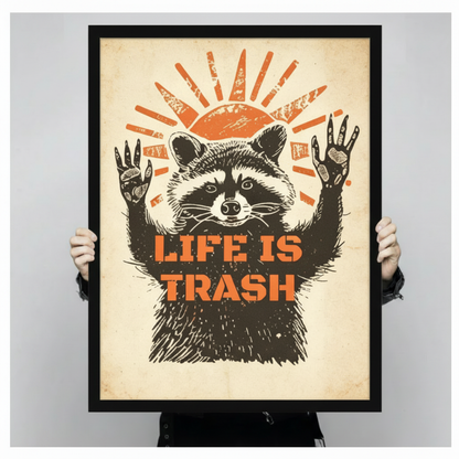 Two hands holding a large black framed retro linocut raccoon with raised arms and resigned expression under an orange woodcut sun with bold Life Is Trash stencil text vintage humor poster canvas art print on aged cream background, front-facing vertical product size display
