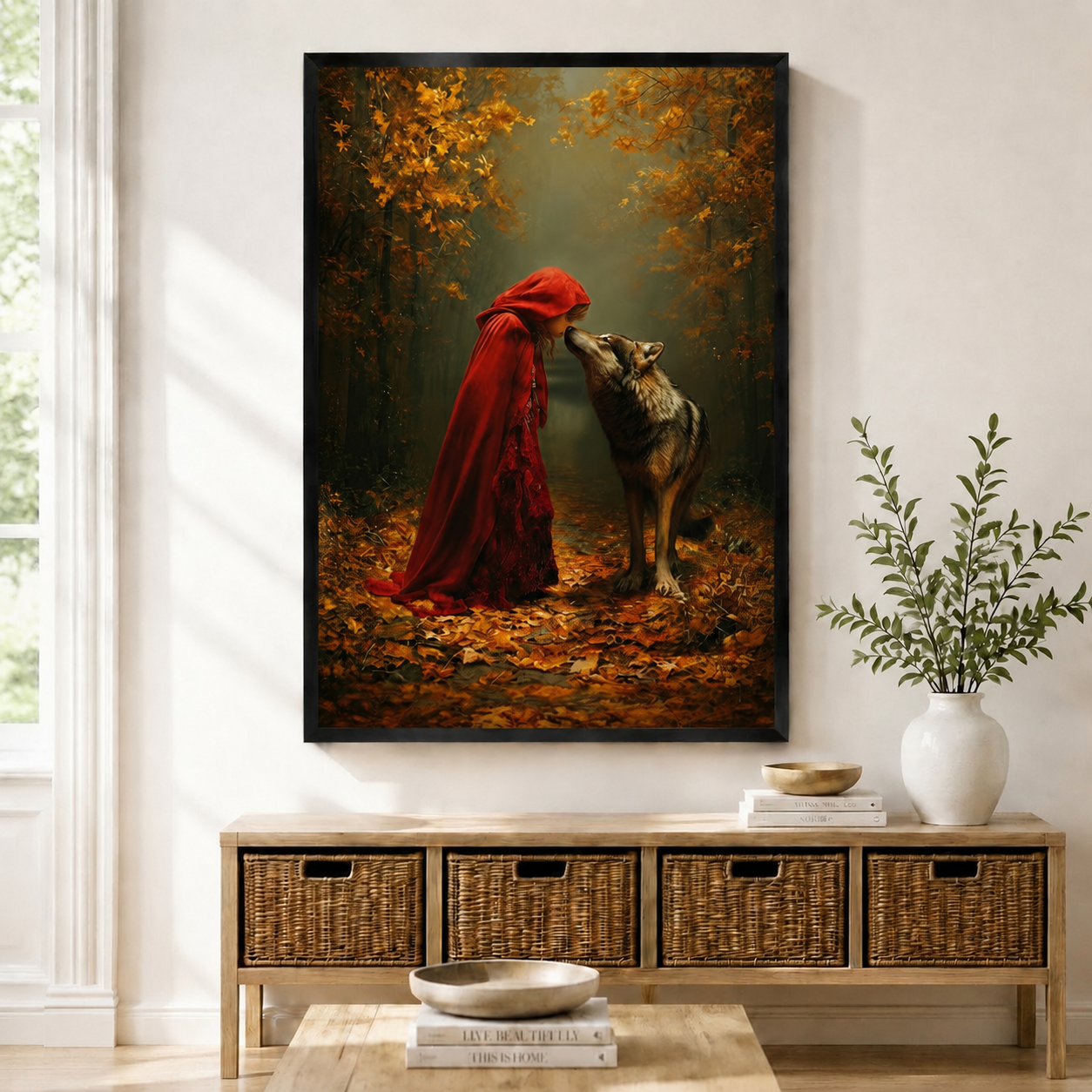 Framed fantasy wall art print of Red Riding Hood in a crimson cloak facing a wolf in an autumn forest, displayed above a wicker console in a bright entryway