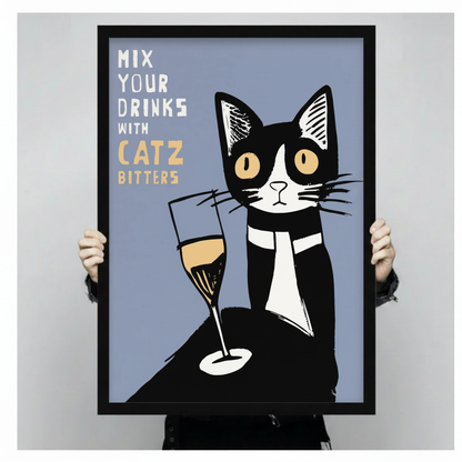 Hands holding a large black framed retro poster style tuxedo cat with champagne glass Mix Your Drinks With Catz Bitters canvas art print with a bold graphic black and white tuxedo cat with large round amber eyes beside a tall champagne flute with golden liquid on a muted slate blue background with white and gold hand-lettered quote