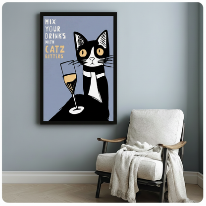 Black framed retro poster style tuxedo cat with champagne glass Mix Your Drinks With Catz Bitters canvas art showing a graphic black and white tuxedo cat with wide amber eyes next to a tall champagne flute with golden liquid on a muted slate blue background with white and gold hand-lettered text, displayed beside a white linen wood-frame armchair with a cream throw