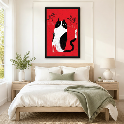 Black framed retro folk art tuxedo cat and two birds canvas art with a black and white cat sitting upright with a deadpan expression and two small line-drawn birds above on a vivid red distressed background, hung above a wooden bed frame in a sun-drenched Scandinavian bedroom with crisp white linen bedding, a sage green accent pillow, matching round nightstand lamps, and a white ceramic vase of greenery