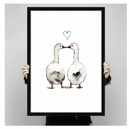 Hands holding a large black framed canvas print of two white geese touching beaks with a heart drawn above them in fine line art, ink wash illustration on white background against a light gray backdrop