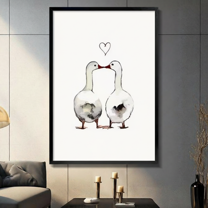 Two white geese touching beaks beneath a hand-drawn heart, watercolor ink illustration on cream background, black framed canvas wall art above a dark console table with pillar candles and black vase against a gray paneled wall
