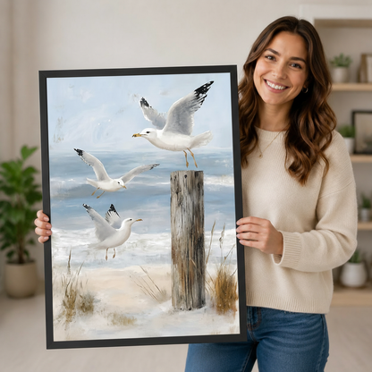 Smiling woman holding a large framed seagull beach wall art print with soft blue, white, and sand tones, showing black frame finish and print scale against a neutral home interior background
