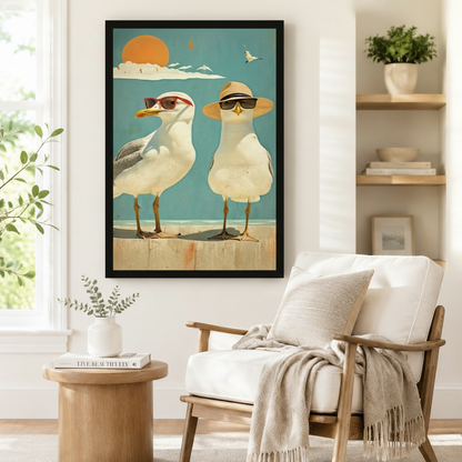 Black framed vintage-style seagull duo in sunglasses and sun hat beach scene wall art hung beside a white linen armchair and round wood side table in a bright Scandinavian living room