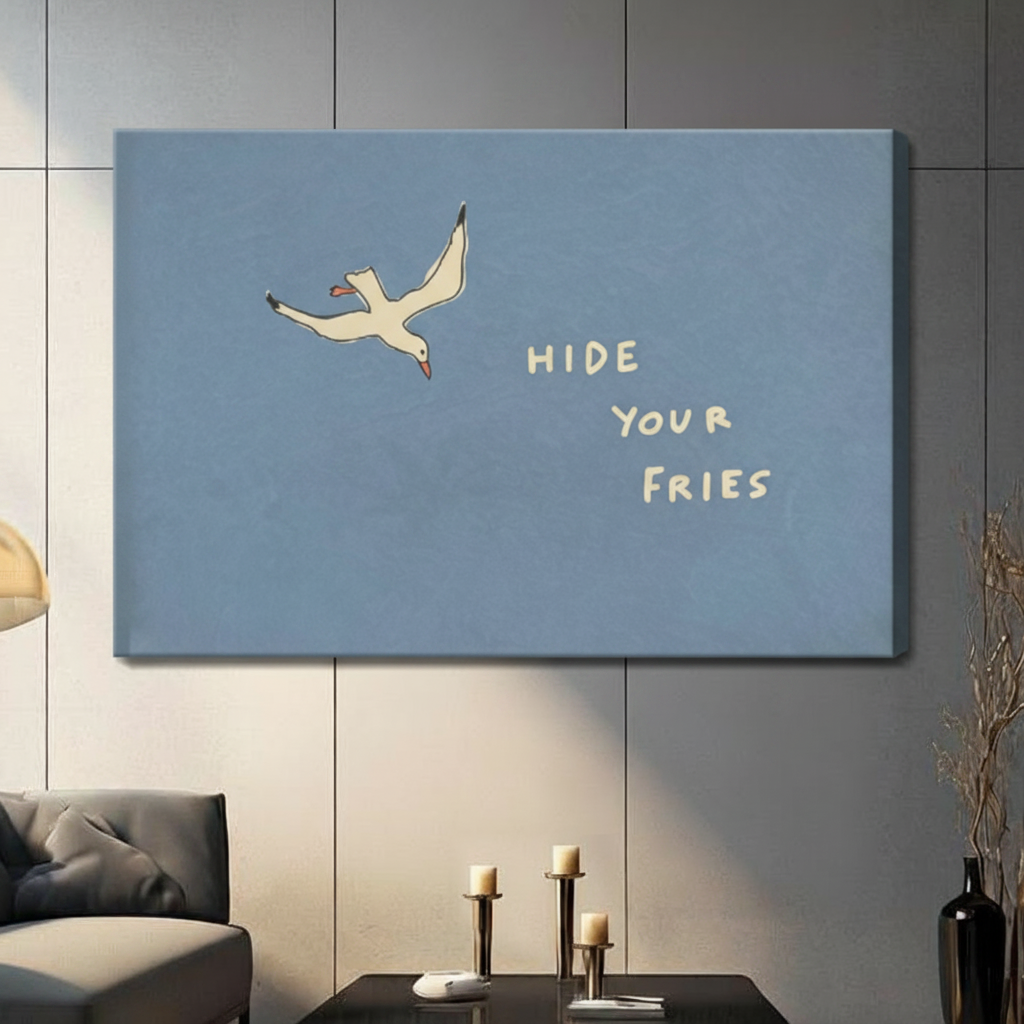 Gallery wrap stretched canvas of a flying white seagull with Hide Your Fries handwritten quote on a powder blue background hung frameless on a dark gray paneled wall above candlestick holders