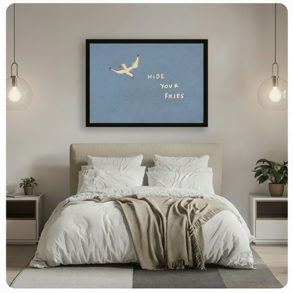 Black framed funny seagull Hide Your Fries coastal quote canvas wall art hung above a beige upholstered bed with white linen bedding in a minimalist bedroom with glass globe pendant lights and potted plants