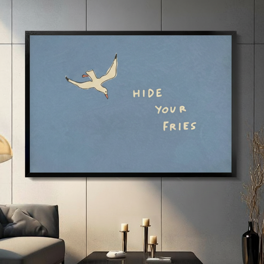 Black framed Hide Your Fries seagull funny quote canvas wall art with dusty blue background displayed in a modern dark gray living room with gray sofa, candlestick holders and tall black vase