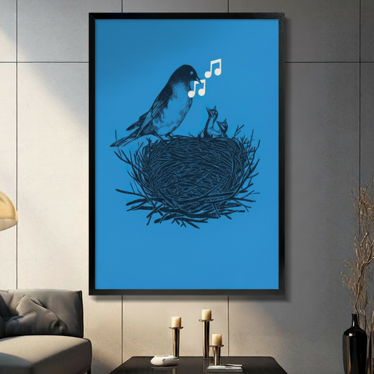 Black framed canvas print of mother bird singing to baby chicks in nest with white music notes on vivid blue background, displayed on grey wall above console table with candles