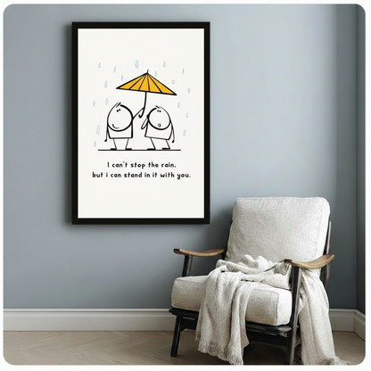 Black framed minimalist friendship in rain canvas art print with two round cartoon characters under a yellow umbrella and the heartfelt quote I can't stop the rain but I can stand in it with you on a blue-grey wall beside a white linen armchair with throw