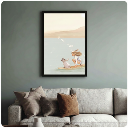 	Black-framed poster of a girl and her French bulldog surfing together on a warm beige and teal watercolor background, hung above a linen sofa