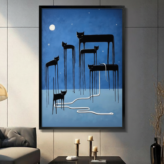 Black framed surreal black cats with impossibly long dripping legs standing beneath a glowing full moon on a deep blue night sky canvas art with a white serpent weaving between them, displayed on a gray tile wall above a console table with gold candlesticks beside a charcoal sofa