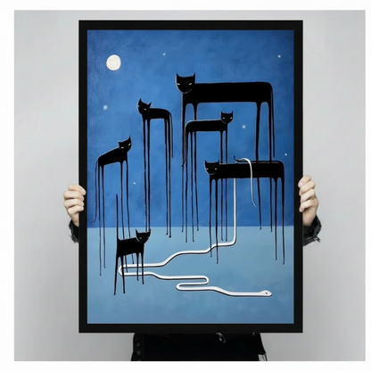 Person holding up a large black framed surreal black cat moon canvas art print showing five eerie elongated cats with dripping melting legs standing on a deep blue night landscape with a glowing full moon and a white snake slithering between them against a light gray background