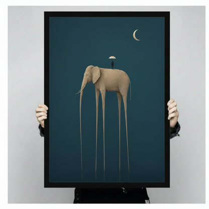 Person holding a large black framed surrealist canvas art print depicting a golden long-legged elephant with a tiny figure under an umbrella against a deep teal background with a crescent moon in the upper right corner, showcasing print size and frame quality