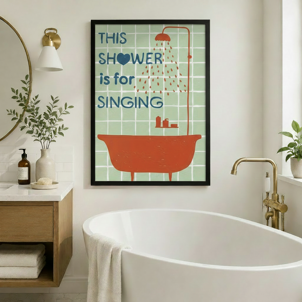 Framed retro bathroom wall art print reading "This Shower is for Singing" with a bold orange bathtub illustration on mint green tiles, hung on a white wall beside a freestanding soaking tub with gold fixtures