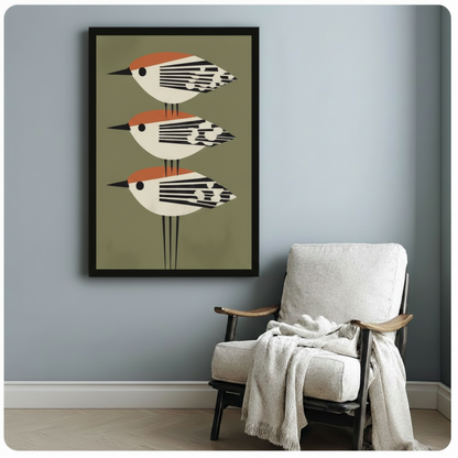 Framed geometric bird poster with olive green background displayed beside a linen armchair on a light blue-grey wall