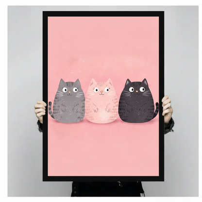 Hand-held black framed art print featuring three cute round cats on blush pink background close-up product display