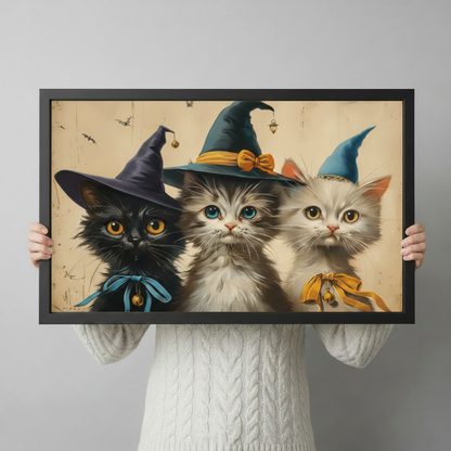 Cute vintage Halloween poster of three kittens wearing colorful witch hats with bows and bells a black cat a fluffy gray-white cat and a white cat grouped together on a distressed beige background with small bat silhouettes whimsical Halloween witch cat wall art framed print held up against a light gray background