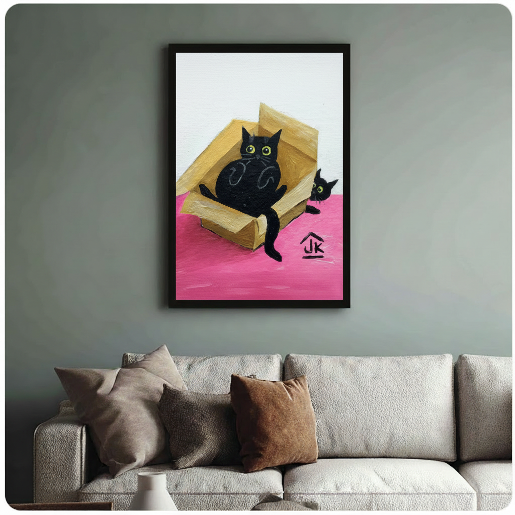 Whimsical oil painting of two black cats with bright green eyes sharing a cardboard box on a vivid pink surface, black framed print above beige fabric sofa in sage green living room