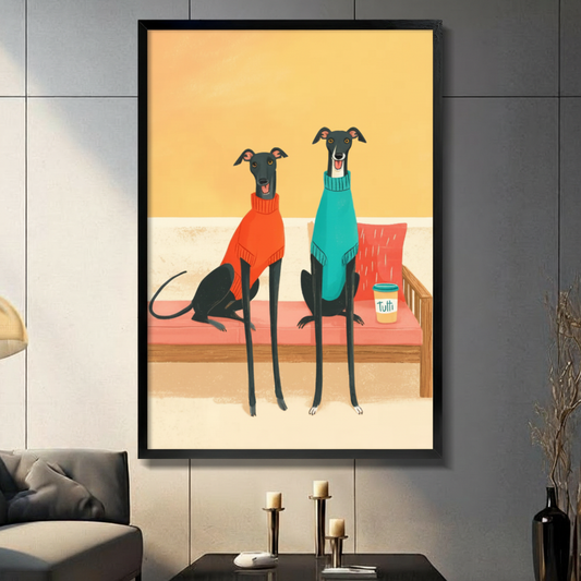 Framed canvas wall art featuring two black greyhounds wearing colorful sweaters sitting on a pink sofa, whimsical dog illustration displayed in a modern living room