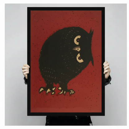 Person holding a black framed vintage Japanese chubby black owl art print on deep red background against a light gray backdrop showing full artwork detail with golden crescent eyes