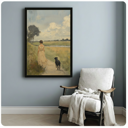 Framed pastoral oil painting style print of a woman and black dog on a country trail, styled beside a cozy armchair on a blue-grey wall