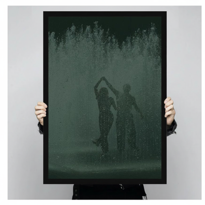 Dancing couple in green fountain spray in black framed canvas held by a person.