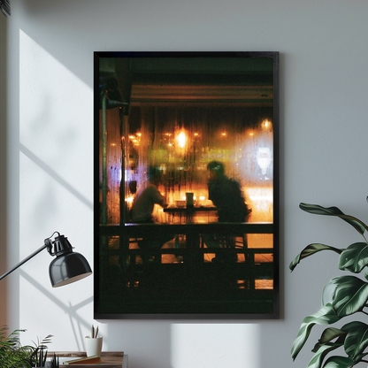 Warm cafe silhouettes behind a rainy window displayed in black framed canvas beside a lamp.