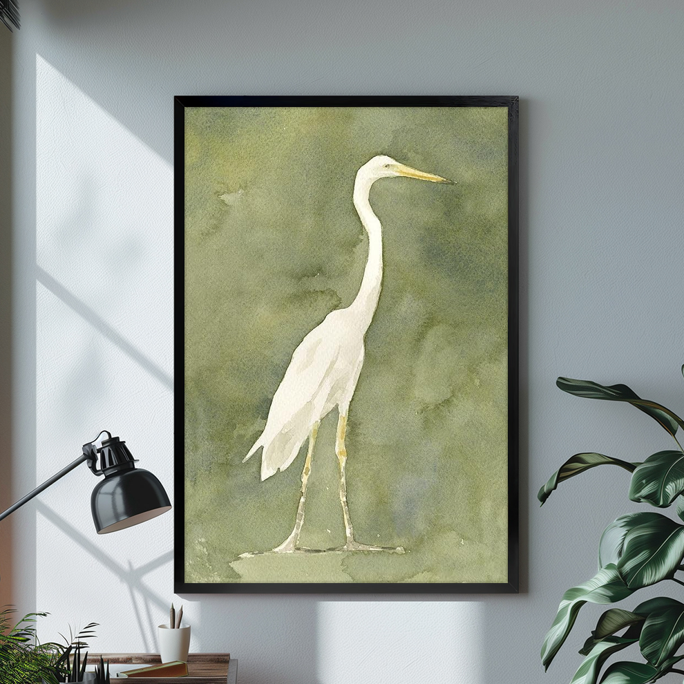 White heron watercolor on an olive background displayed in black framed canvas beside a lamp.