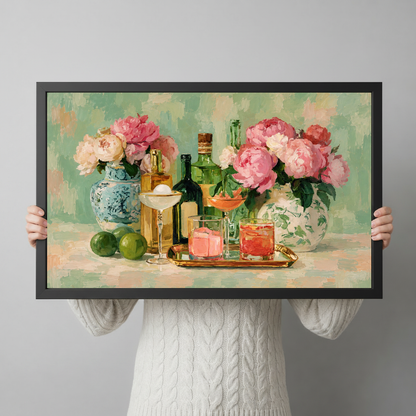 Person holding black framed floral cocktail artwork with pink peonies and colorful glasses.