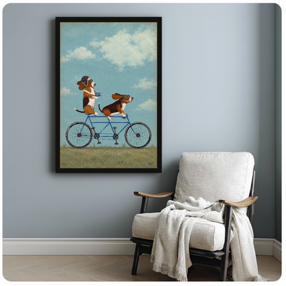 Framed tandem bicycle beagles artwork beside a pale reading chair against a blue-gray wall.