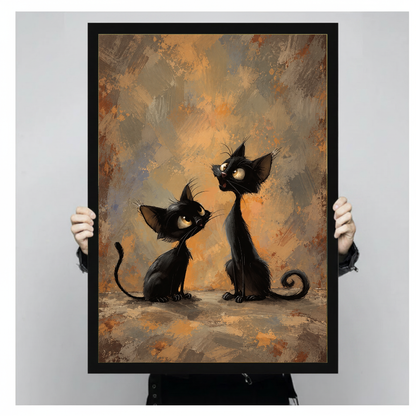 Framed artwork of two curious black cats with curled tails held by a person against a pale backdrop.
