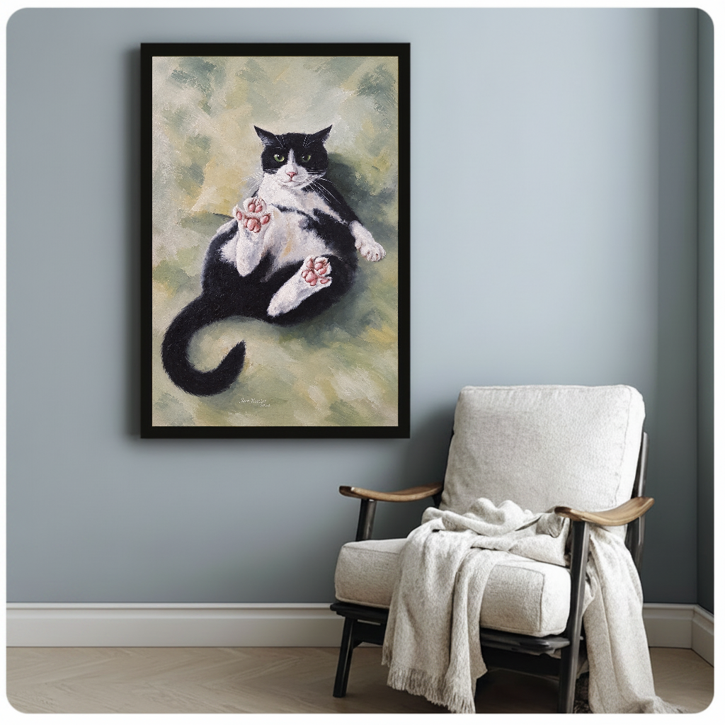Framed relaxed tuxedo cat artwork beside a pale reading chair against a blue-gray wall.