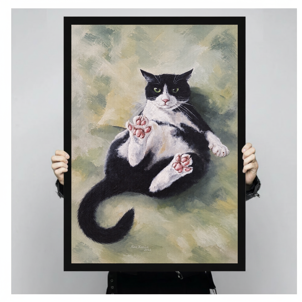 Person holding black framed relaxed tuxedo cat artwork against a plain pale background.