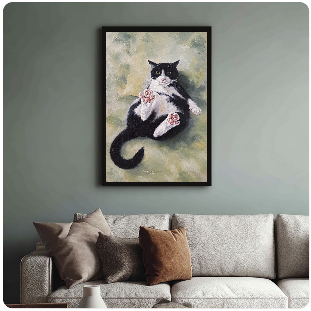 Framed relaxed tuxedo cat painting above a sofa with muted cushions against a green-gray wall.