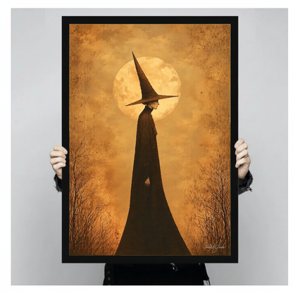 Person holding black framed golden moon witch artwork against a plain pale background.