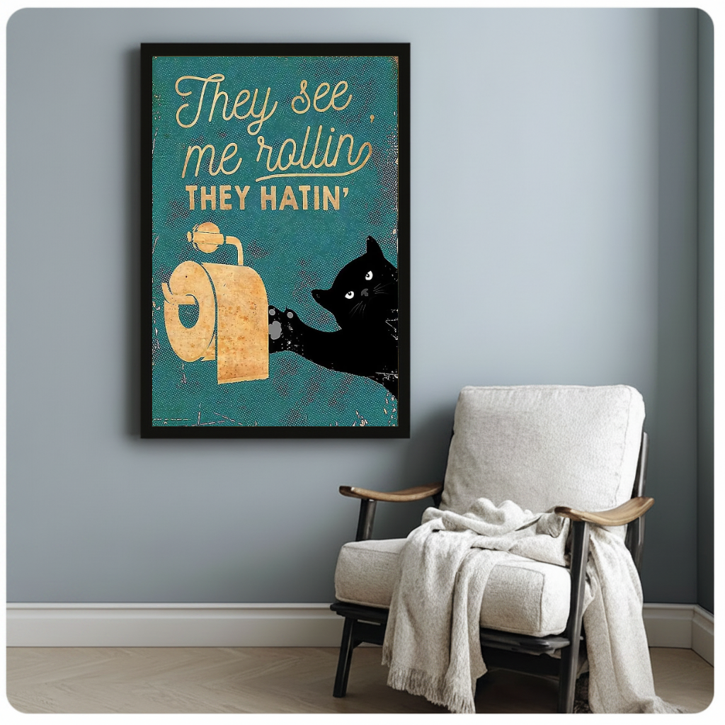Framed teal toilet paper cat artwork beside a pale reading chair against a blue-gray wall.
