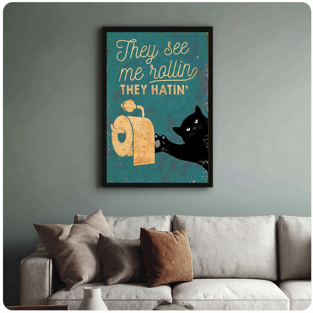 Framed teal toilet paper cat painting above a sofa with muted cushions against a green-gray wall.