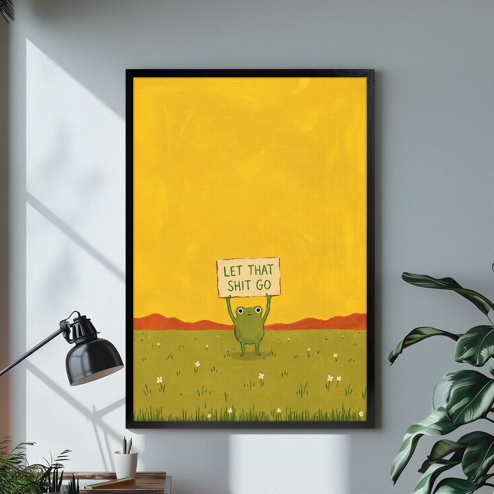 Black framed canvas depicting a green frog holding a humorous sign on a bright desk with a lamp.