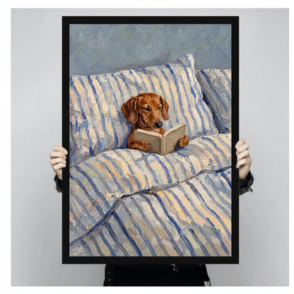 Framed artwork of a dachshund reading in a striped bed held by a person against a pale backdrop.