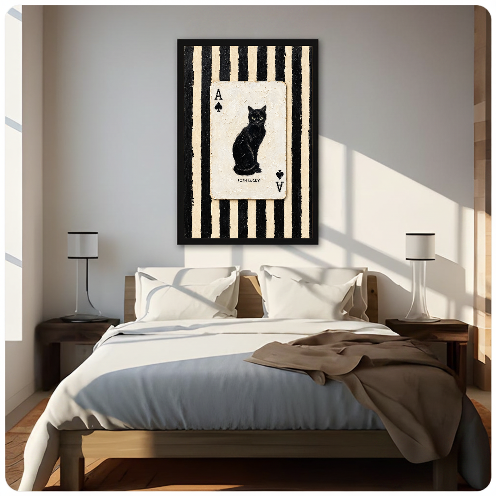 Framed artwork of a black cat inside an ace playing card above a neutral bed between two bedside lamps.