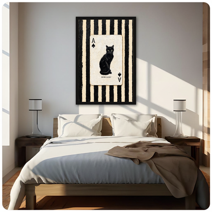Framed artwork of a black cat inside an ace playing card above a neutral bed between two bedside lamps.
